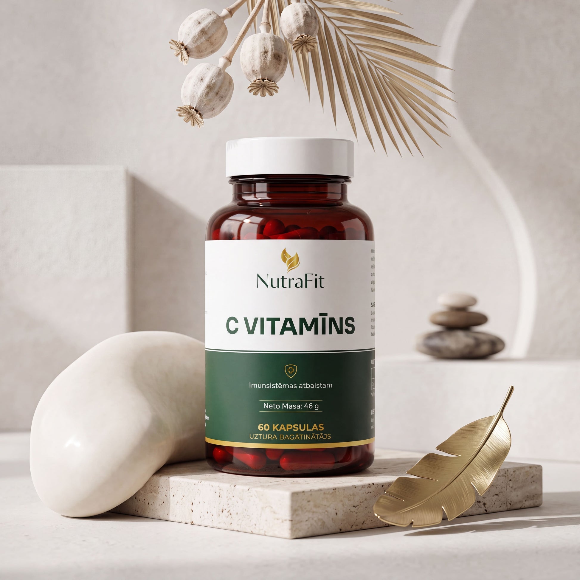 A bottle of NutraFit C Vitamins dietary supplement, styled on a light stone pedestal with decorative props including a gold feather, white stones, and dried pods against a neutral beige background.